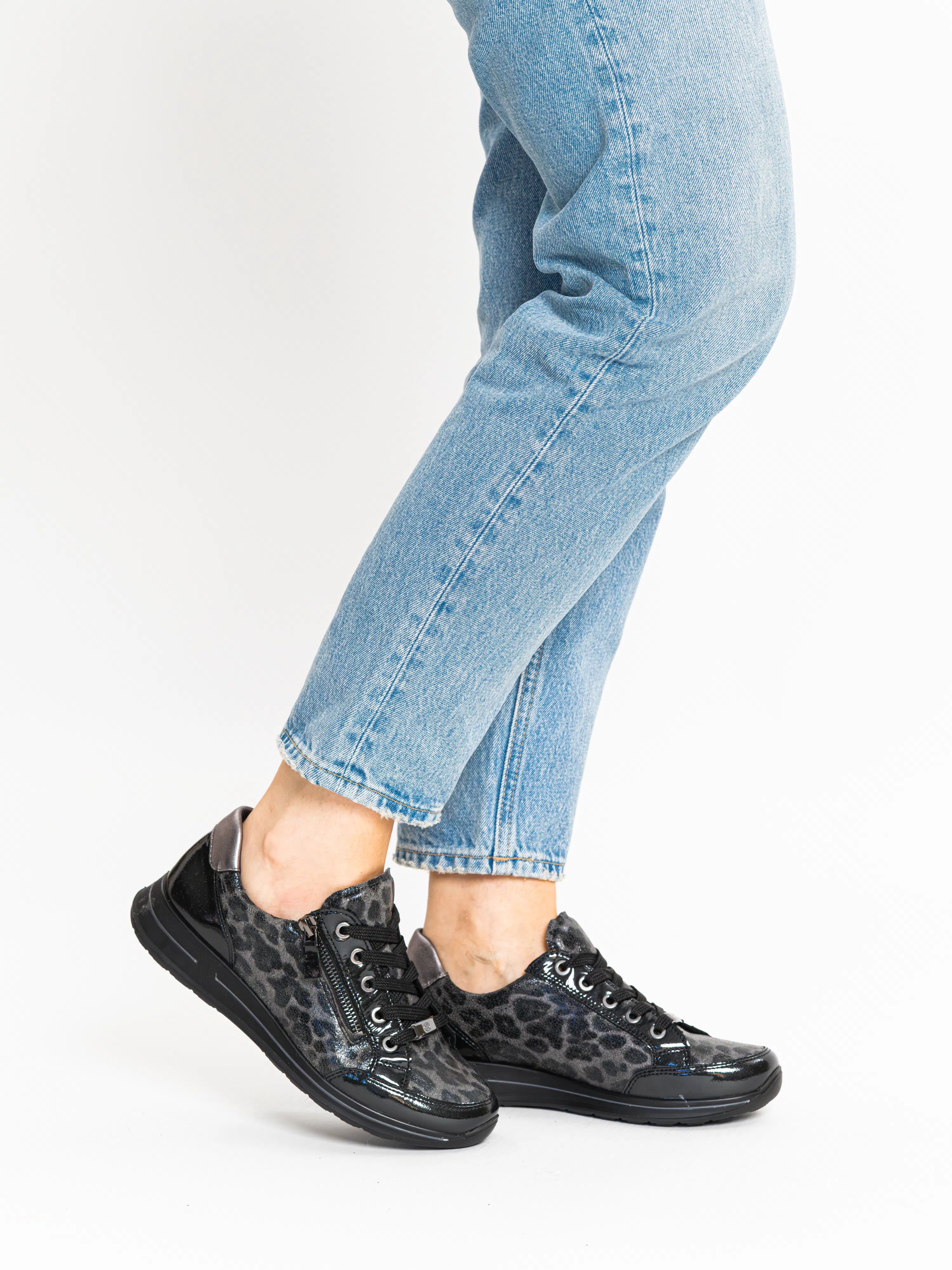 Person wearing black leopard print sneakers with light blue jeans on a white background