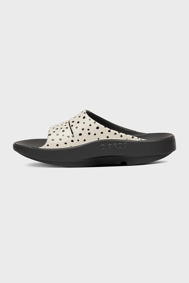 OOFOS OOahh Women's Slide Sandal Pebble Black sandal with white polka dot design on a light gray background