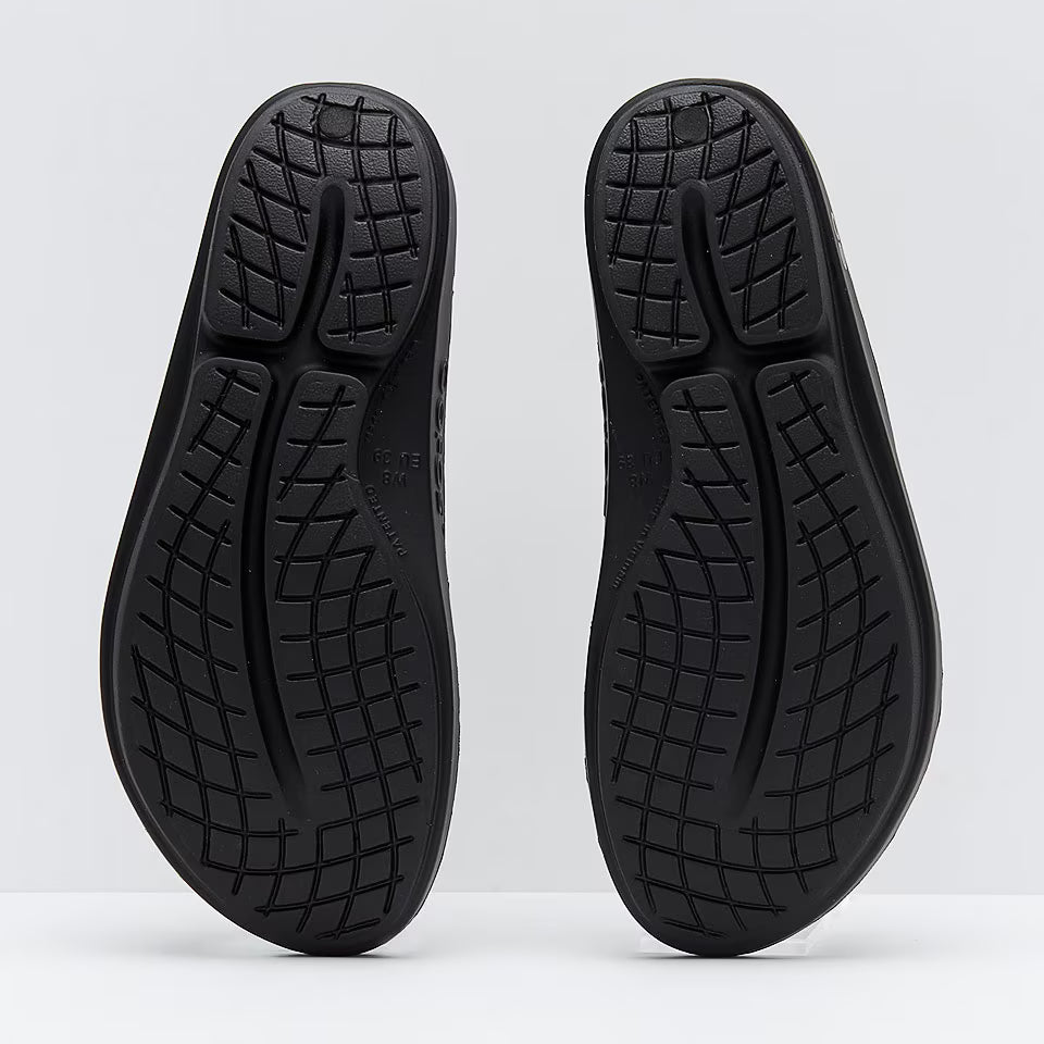 OOFOS Oolala Recovery Flip-Flops Thong sport active black sandals soles with tread pattern on a white background